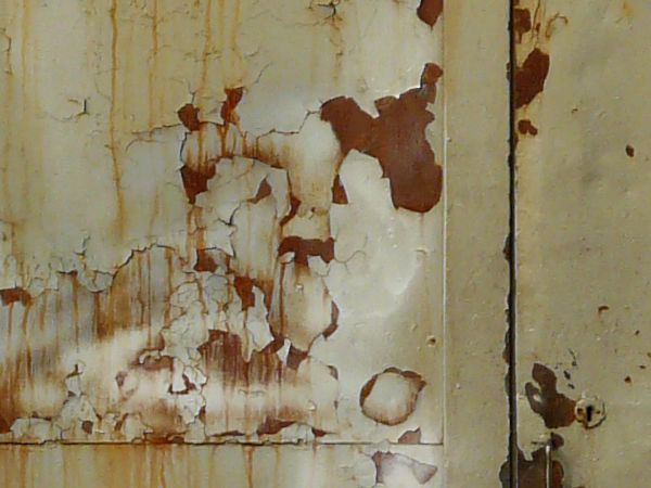 Large aged beige doors with crumbling paint and rusting surface.